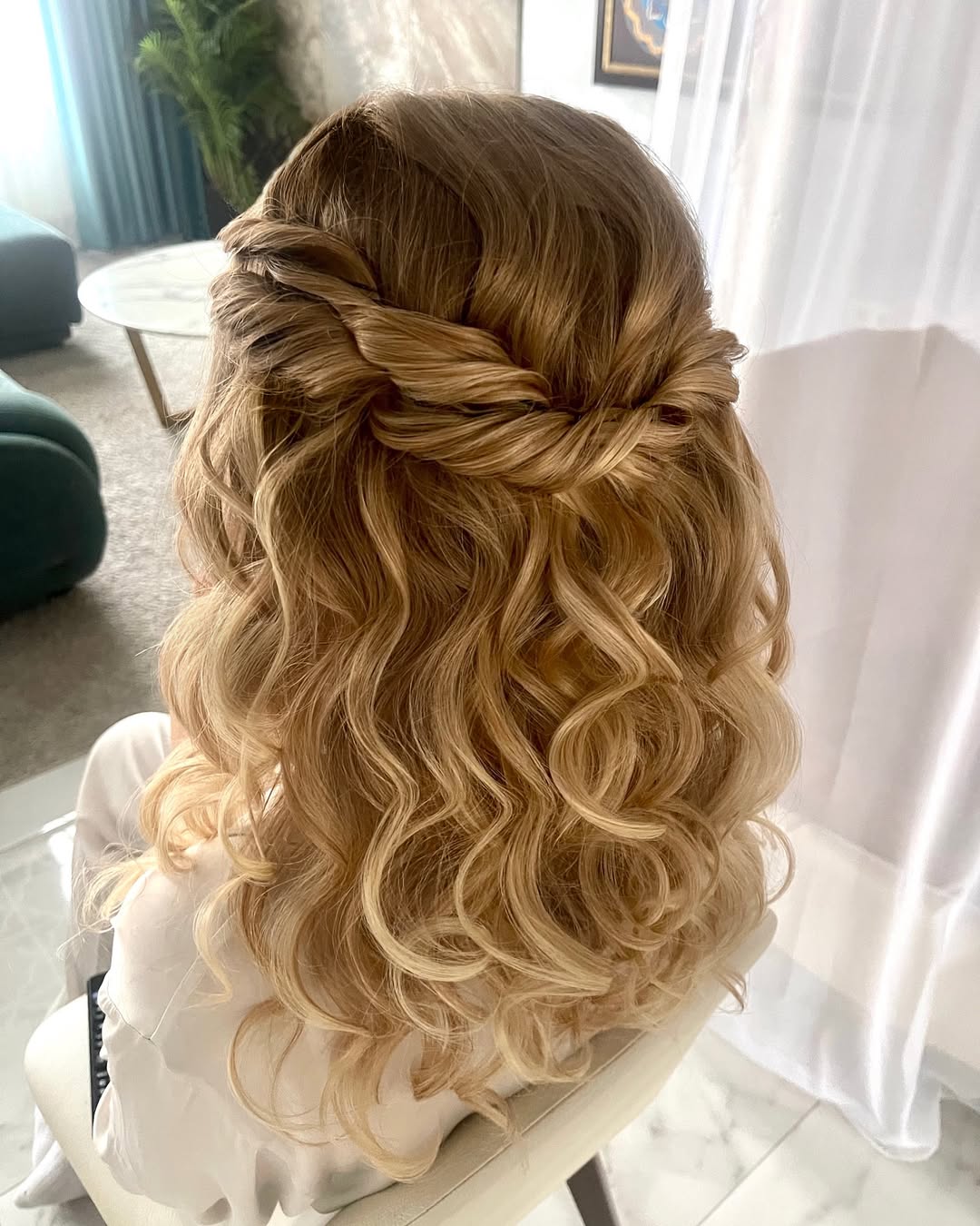 Blonde teenage girl with long wavy hair tied into a half-up, half-down style with face-framing pieces, perfect for summer hairstyles teenage girls 2026. She wears a casual white t-shirt and small hoop earrings.