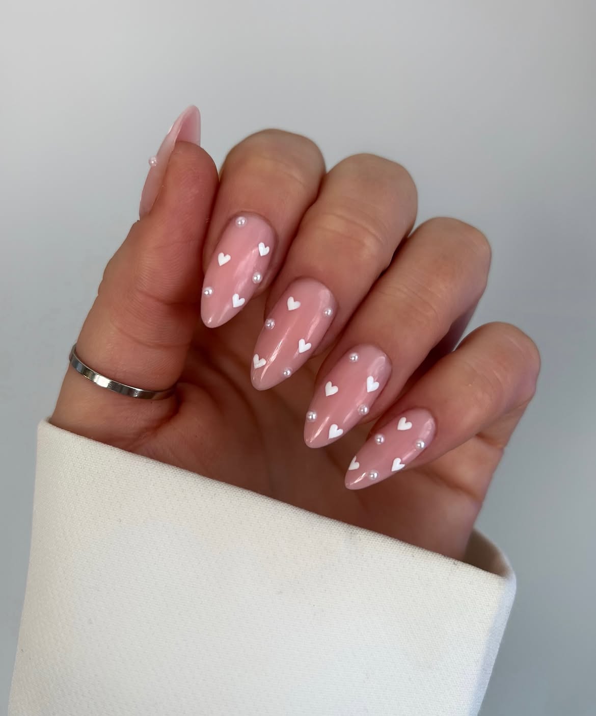 Glossy Nude Almond Nails With White Hearts And Pearls